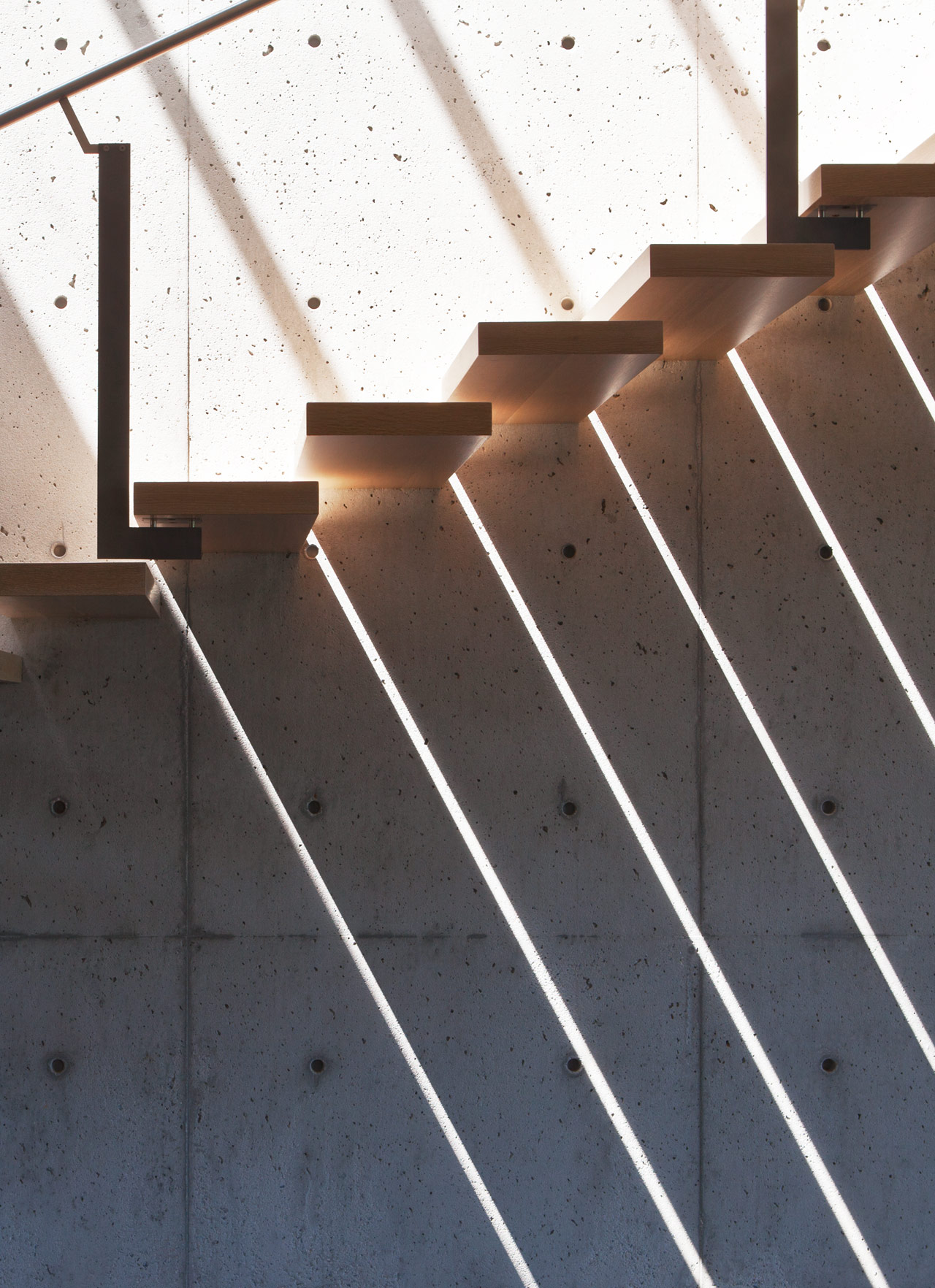 Light shining through slits in floating wood staircase against concrete wall.